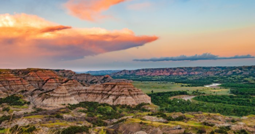 A scenic landscape featuring layered hills, a river, and a colorful sunset sky with clouds.