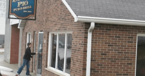 A person approaches the entrance of a brick building with a sign reading "Lucky Pig Pub & Grill."