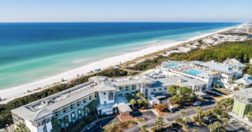 Aerial view of a coastal resort with a pool, surrounded by white sand beaches and turquoise waters.