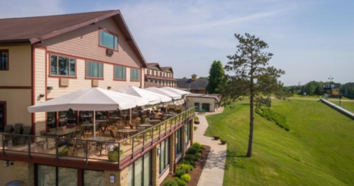A modern building with a patio and umbrellas, overlooking a green lawn and golf course under a clear blue sky.