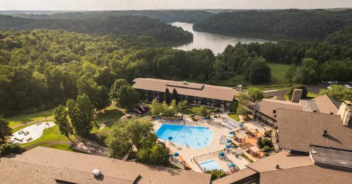 Aerial view of a resort with a pool, surrounded by trees and a lake in the background.