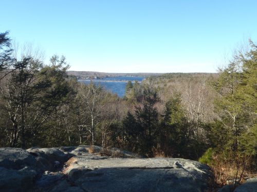 A scenic view of a lake surrounded by trees and hills under a clear blue sky.