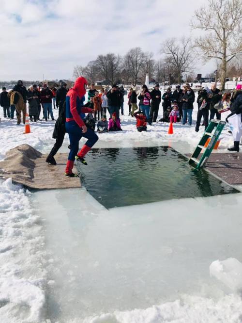 A person in a Spider-Man costume steps onto a platform by a partially frozen pool, with a crowd watching nearby.