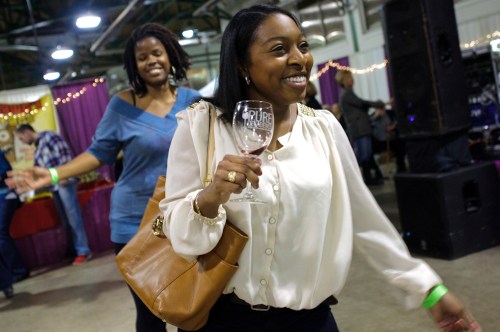 Two women enjoy a lively event, one holding a wine glass and smiling, while the other dances in the background.