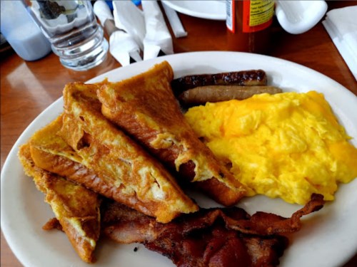 A plate of breakfast featuring French toast, scrambled eggs, sausage, and bacon.