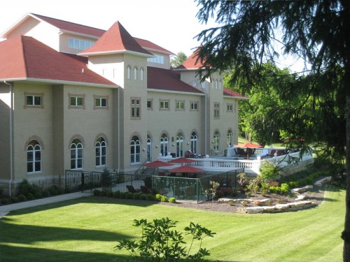 A large, elegant building with a red roof, surrounded by green lawns and landscaped gardens.
