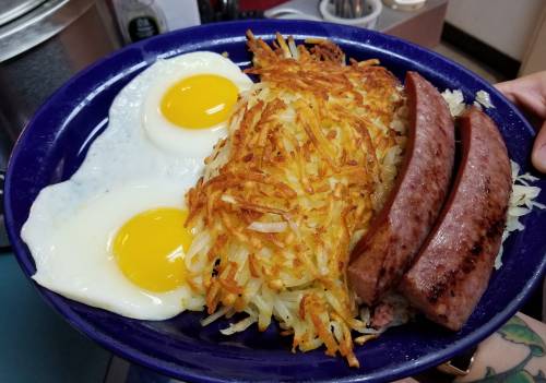 A blue plate with two sunny-side-up eggs, crispy hash browns, and two slices of sausage.