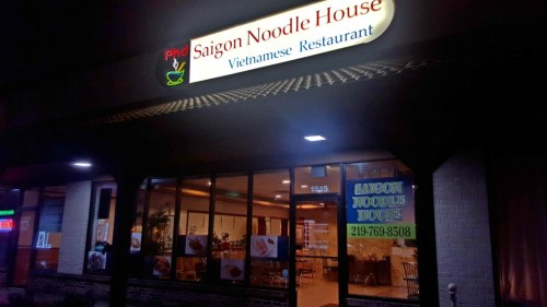 Exterior of Saigon Noodle House, a Vietnamese restaurant, with illuminated sign and large windows at night.