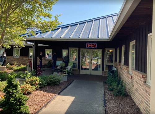 A building with a blue metal roof and an "OPEN" sign, surrounded by greenery and a pathway.
