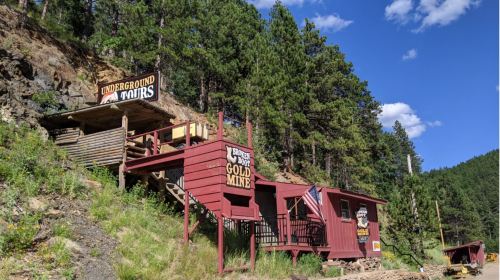 A rustic building labeled "Gold Mine" surrounded by trees and mountains, with a sign for underground tours.