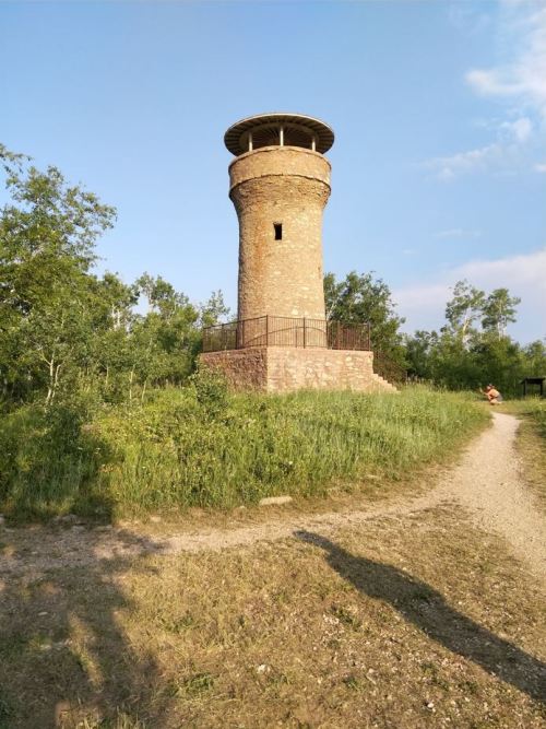 A stone observation tower surrounded by greenery, with a path leading up to it under a clear blue sky.