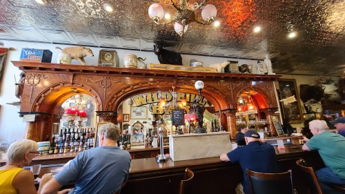 Interior of a rustic bar with wooden decor, vintage memorabilia, and patrons seated at the counter.