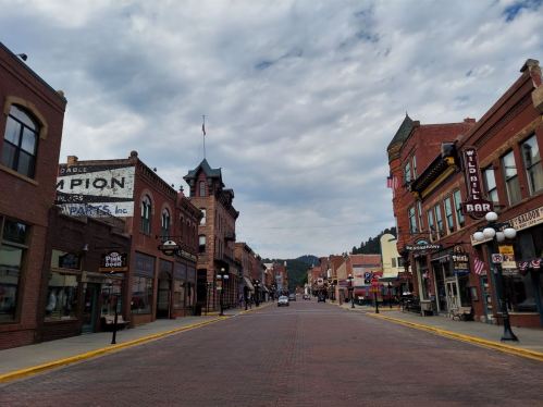 Historic street view of a small town with brick buildings, shops, and a cloudy sky.