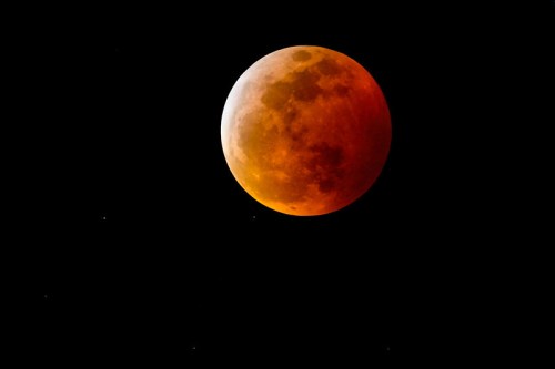 A glowing orange moon partially obscured against a black sky, with faint stars visible around it.