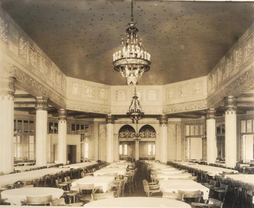 Elegant dining hall with round tables, ornate chandeliers, and decorative columns, captured in vintage style.