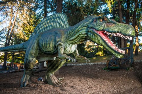 A large, realistic dinosaur sculpture stands among trees, showcasing its sharp teeth and detailed scales.