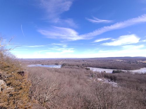 A panoramic view of a winter landscape with bare trees, a lake, and a clear blue sky.