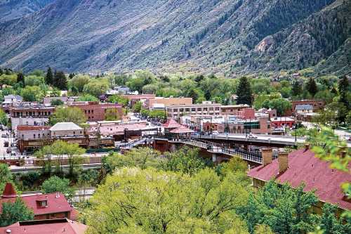 A scenic view of a small town nestled in green hills, featuring buildings and a bridge surrounded by lush trees.