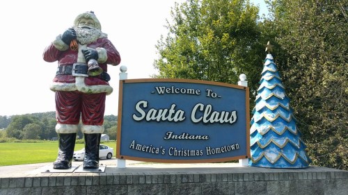Welcome sign for Santa Claus, Indiana, featuring a large Santa statue and a decorated Christmas tree.