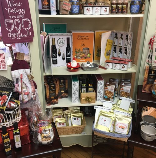 A display of gourmet food products, wine, and gift items on shelves in a cozy shop setting.