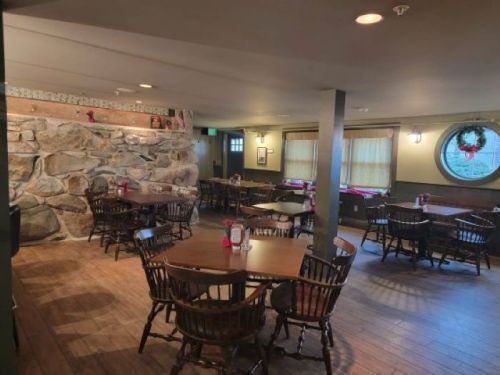 Cozy restaurant interior with wooden tables, chairs, and a stone wall, featuring warm lighting and festive decorations.