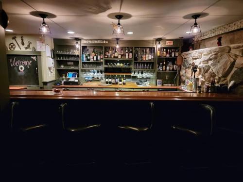 A dimly lit bar with a wooden counter, shelves of bottles, and a stone wall in the background.