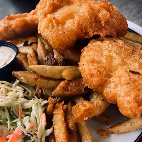 A plate of golden fried fish fillets served with crispy fries and a side of coleslaw.