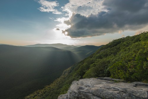 A scenic view of mountains under a cloudy sky, with sunlight breaking through and illuminating the landscape.