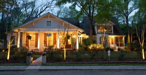 A charming house illuminated at dusk, surrounded by trees and a well-kept garden, with a welcoming front porch.