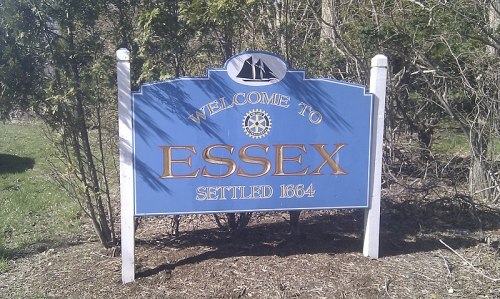 Welcome sign for Essex, established in 1664, featuring a nautical design and surrounded by greenery.