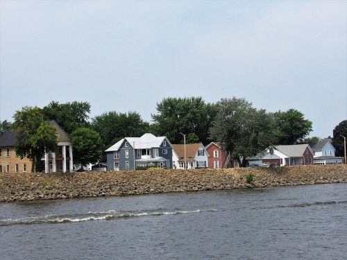 A scenic view of a riverbank lined with colorful houses and lush trees under a cloudy sky.