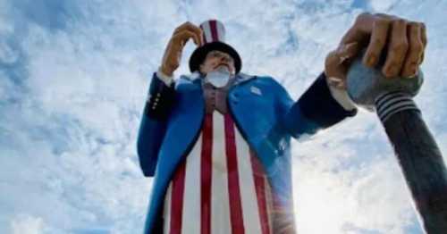 A towering statue of Uncle Sam holding a baseball bat against a cloudy sky.