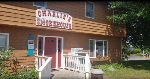 Exterior of Charlie's Smokehouse, a brown building with a sign, open door, and a small ice vending machine outside.