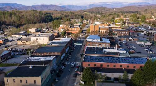 Aerial view of a small town with shops, streets, and mountains in the background under a clear sky.