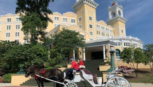 A horse-drawn carriage in front of a large yellow hotel with a tower and lush greenery.