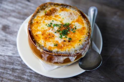 A bowl of French onion soup topped with melted cheese and herbs, served on a plate with a spoon.