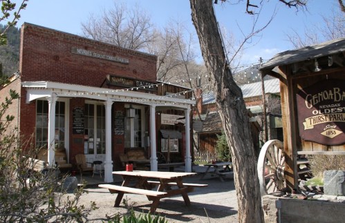 Historic brick building with a porch, surrounded by trees and outdoor seating, labeled as Nevada's oldest thirst parlor.