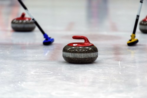 A curling stone on the ice with brooms in the background, ready for a shot in a curling match.