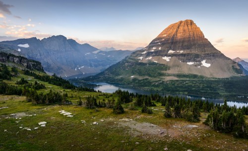 A scenic mountain landscape at sunset, featuring a prominent peak, lush greenery, and a serene lake below.