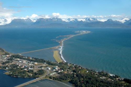 Aerial view of a coastal landscape with mountains, a winding road, and a small town near the water's edge.