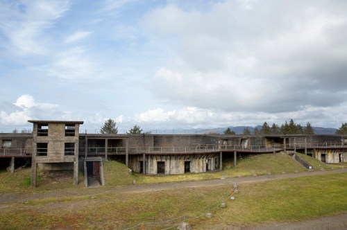 Abandoned concrete structure with multiple levels, surrounded by grassy areas and under a cloudy sky.
