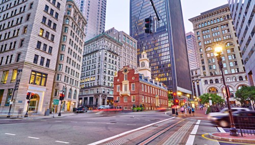 A bustling city intersection with historic and modern buildings, traffic lights, and a hint of evening light.