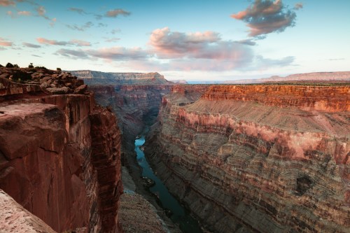 A breathtaking view of a canyon with layered rock formations and a winding river under a colorful sky.
