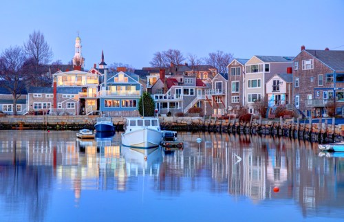 A serene harbor scene at dusk, featuring colorful houses and boats reflecting in calm water.