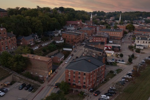 Aerial view of a small town at sunset, featuring historic buildings, streets, and greenery in the background.