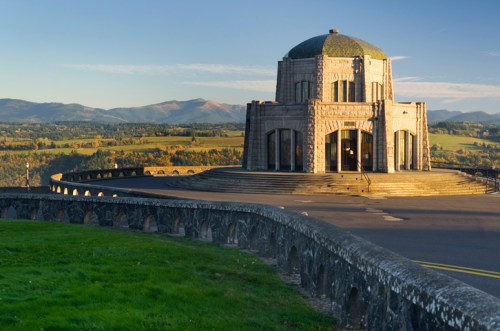 A stone monument with a dome, surrounded by a scenic landscape of hills and fields under a clear sky.