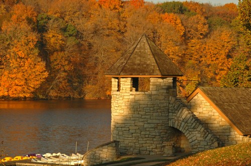 A stone tower by a lake surrounded by vibrant autumn foliage in warm colors.