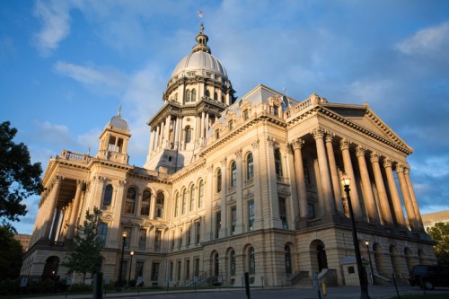 Historic building with a large dome and columns, illuminated by sunlight against a blue sky with clouds.