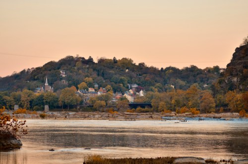 A serene river scene at sunset, with a hillside village and autumn trees reflected in the water.