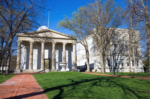 Historic buildings with columns and trees in a green park under a clear blue sky.